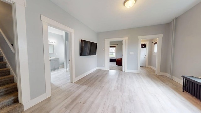 unfurnished living room featuring baseboards, light wood finished floors, and stairs