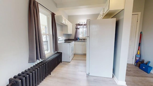 clothes washing area with radiator, light wood-style flooring, cabinet space, and a healthy amount of sunlight