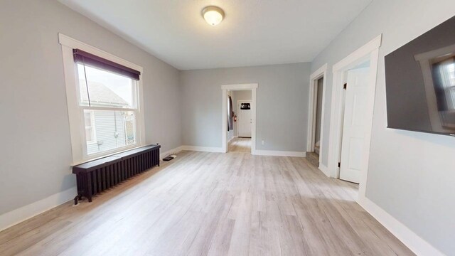unfurnished room with radiator, baseboards, and light wood finished floors
