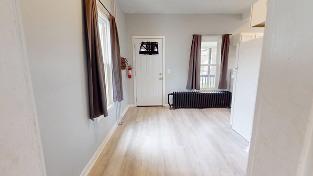 corridor with baseboards, a wealth of natural light, radiator heating unit, and light wood-type flooring