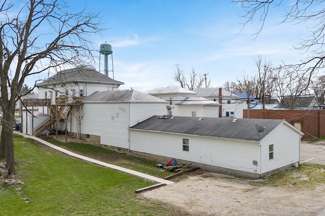 rear view of property with stairs and a lawn
