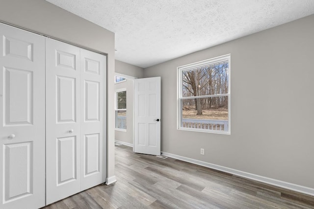 unfurnished bedroom featuring a closet, a textured ceiling, baseboards, and wood finished floors