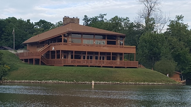 rear view of house with a water view, a chimney, and a lawn