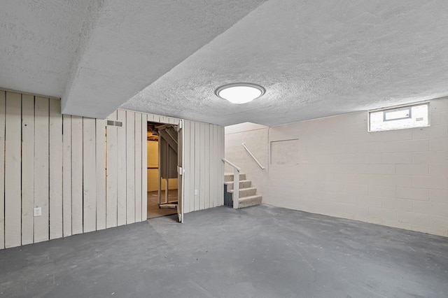 below grade area featuring concrete block wall, visible vents, stairway, and a textured ceiling