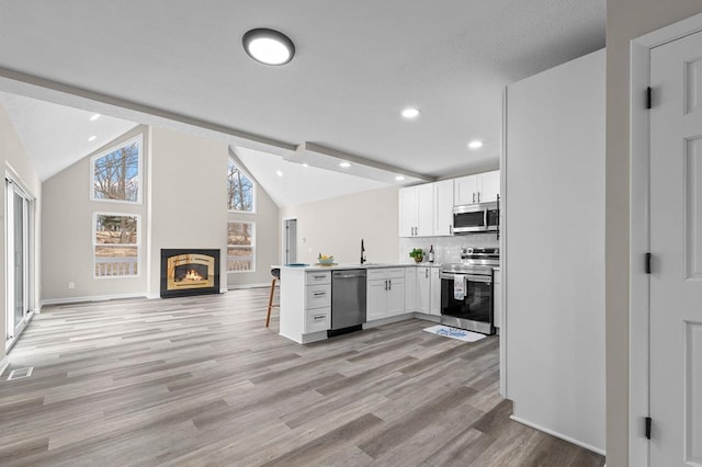 kitchen with lofted ceiling, open floor plan, a peninsula, stainless steel appliances, and white cabinetry