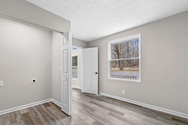 spare room with a textured ceiling, wood finished floors, and baseboards