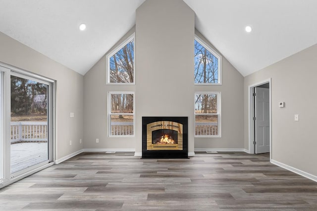 unfurnished living room featuring high vaulted ceiling, a lit fireplace, baseboards, and wood finished floors