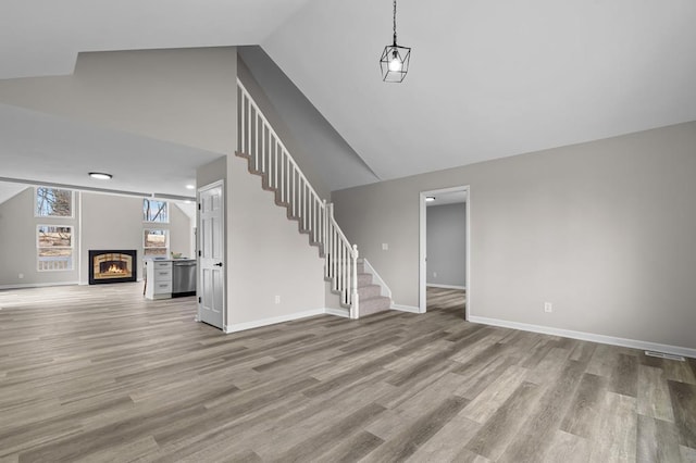 unfurnished living room with a glass covered fireplace, stairway, baseboards, and wood finished floors