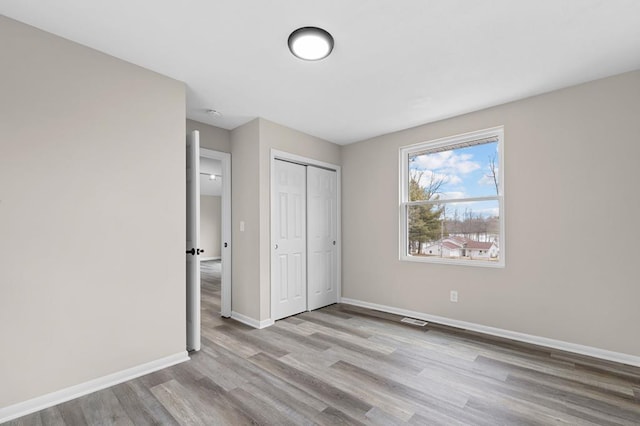 unfurnished bedroom with a closet, wood finished floors, visible vents, and baseboards