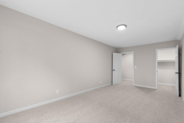 unfurnished bedroom featuring baseboards, a walk in closet, a closet, and light colored carpet