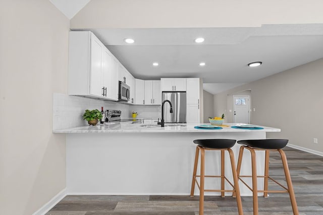 kitchen featuring dark wood finished floors, stainless steel appliances, light countertops, a sink, and a peninsula