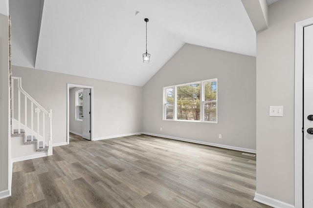 unfurnished living room with stairs, vaulted ceiling, wood finished floors, and baseboards