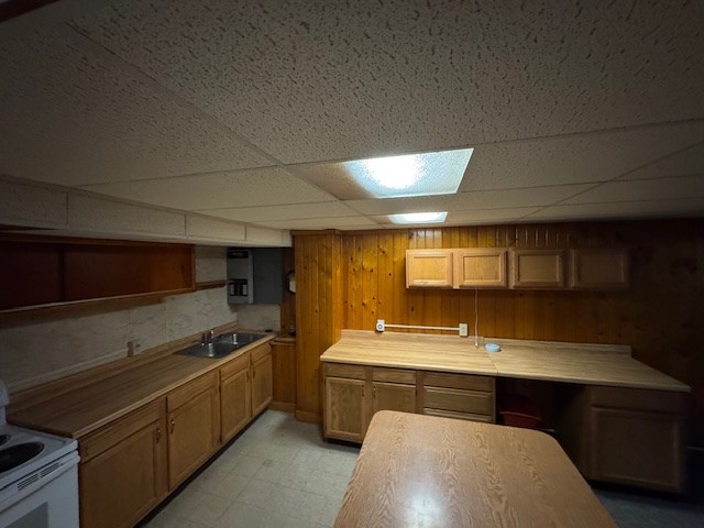 kitchen with a paneled ceiling, wooden walls, sink, and white range with electric cooktop