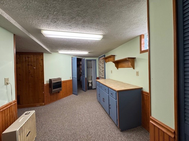 kitchen featuring a textured ceiling, heating unit, wooden walls, and light colored carpet