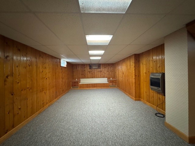 basement featuring heating unit, wooden walls, a drop ceiling, and carpet floors