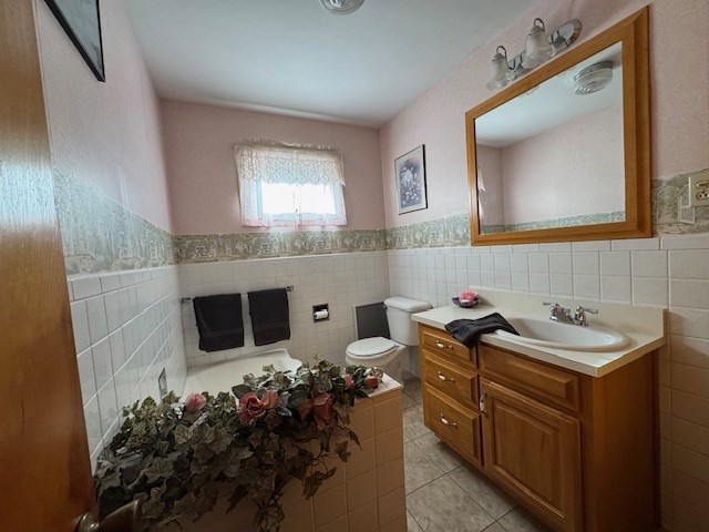 bathroom with toilet, vanity, tile patterned floors, and tile walls