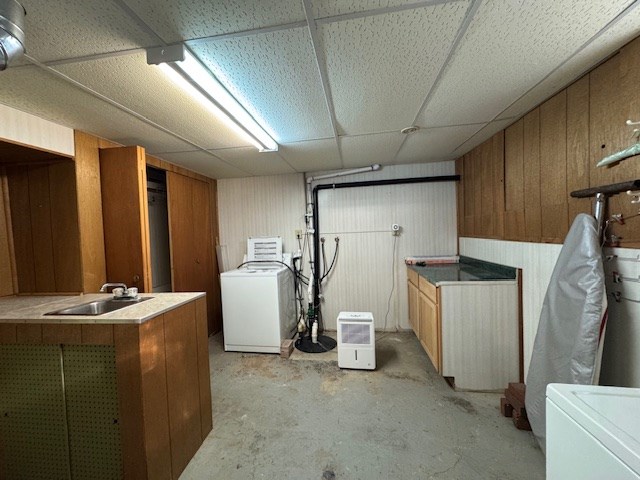 clothes washing area with cabinets, wood walls, washer / dryer, and sink