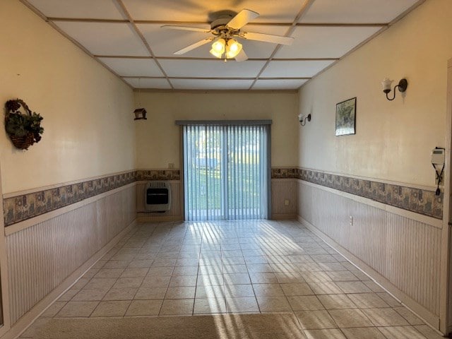 tiled spare room with heating unit, ceiling fan, and wood walls