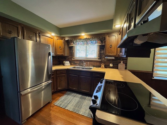 kitchen featuring stainless steel fridge, stove, dark wood-type flooring, exhaust hood, and sink