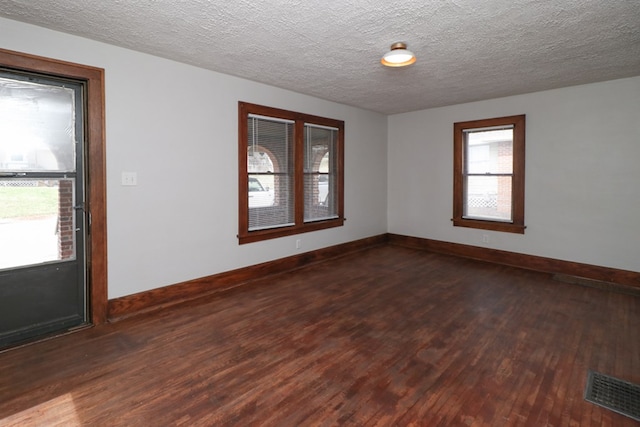 spare room with dark wood-style floors, visible vents, a textured ceiling, and baseboards