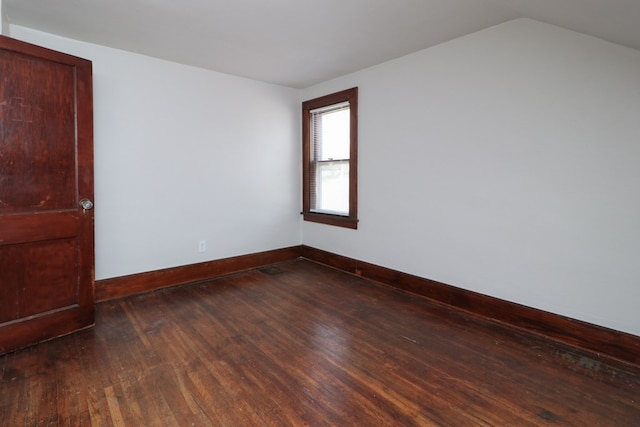 empty room featuring dark wood finished floors, lofted ceiling, and baseboards