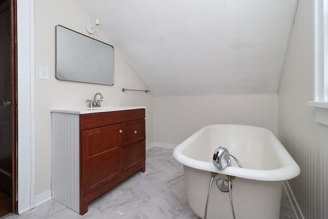 full bath featuring marble finish floor, baseboards, a soaking tub, vanity, and vaulted ceiling