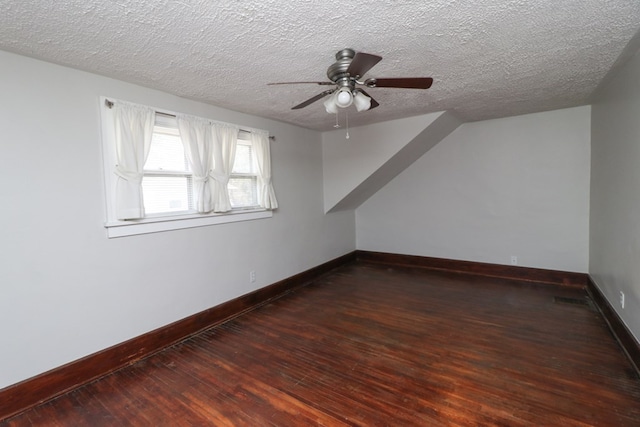 additional living space featuring a textured ceiling, dark wood-type flooring, baseboards, and ceiling fan
