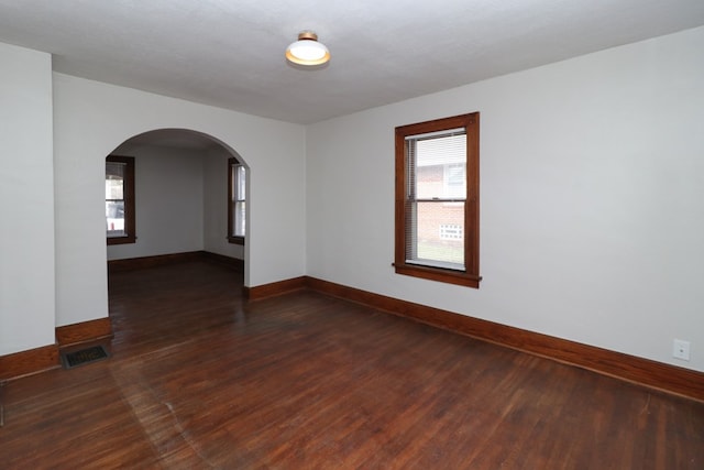 empty room with visible vents, arched walkways, baseboards, and wood finished floors