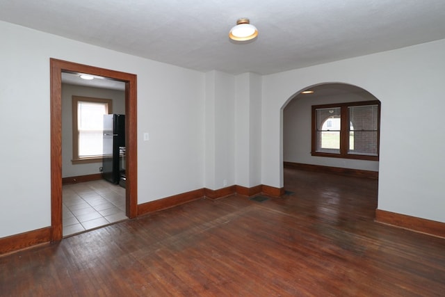 spare room featuring hardwood / wood-style floors, baseboards, and arched walkways