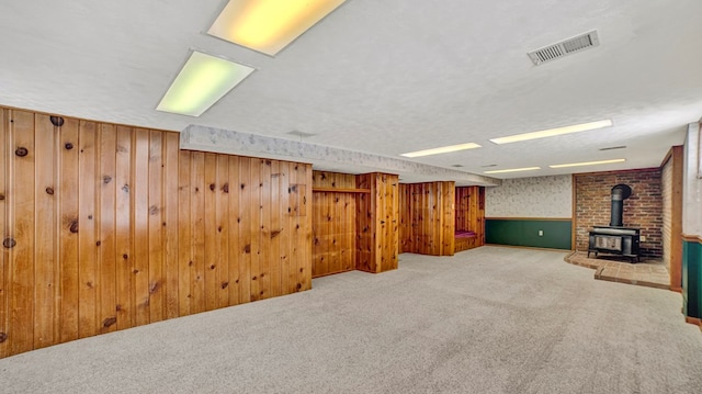 basement with a wood stove, carpet, wood walls, and a textured ceiling