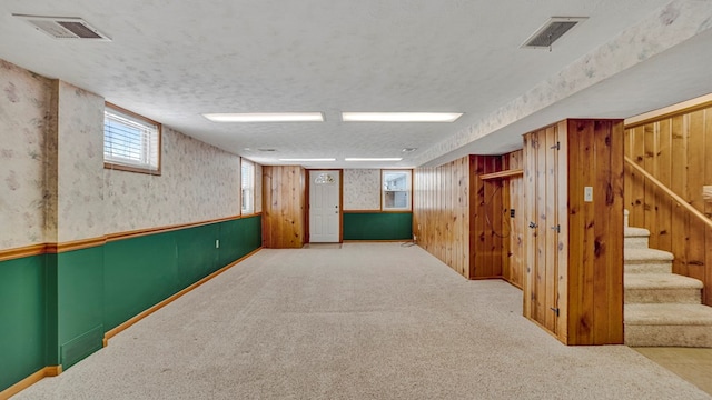 basement featuring carpet floors, a textured ceiling, and wooden walls