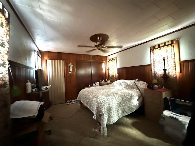 carpeted bedroom with ceiling fan, ornamental molding, and wood walls