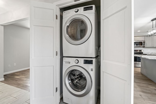 washroom featuring laundry area, baseboards, light wood finished floors, and stacked washing maching and dryer