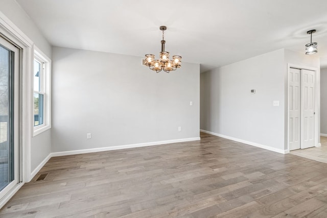 spare room with visible vents, baseboards, light wood-type flooring, and a chandelier