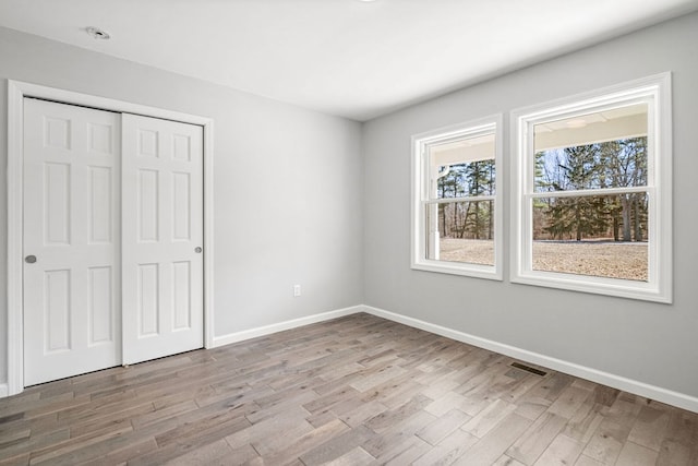 unfurnished bedroom with a closet, visible vents, light wood-type flooring, and baseboards