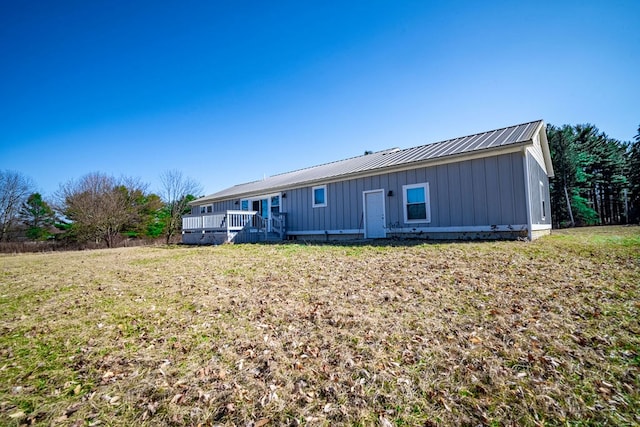 back of house featuring a wooden deck, board and batten siding, metal roof, and a yard