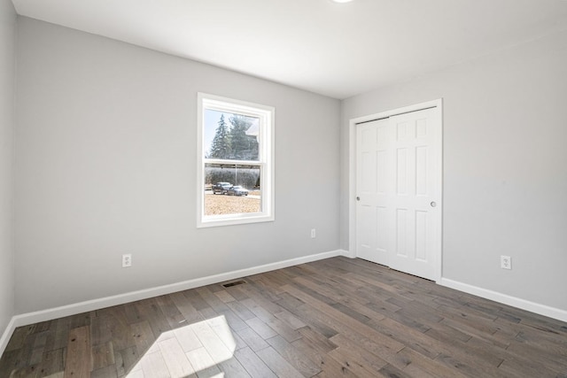 unfurnished bedroom featuring a closet, visible vents, dark wood-type flooring, and baseboards