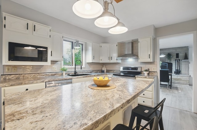 kitchen featuring a kitchen breakfast bar, a sink, white cabinets, stainless steel appliances, and wall chimney exhaust hood