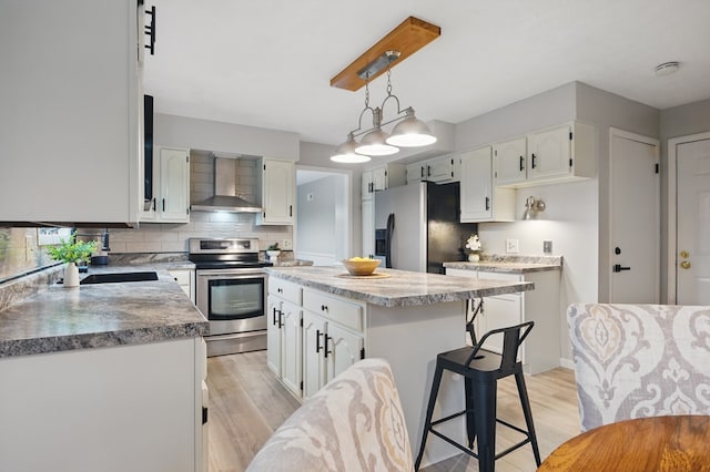 kitchen featuring light wood-style floors, wall chimney exhaust hood, white cabinets, and stainless steel appliances