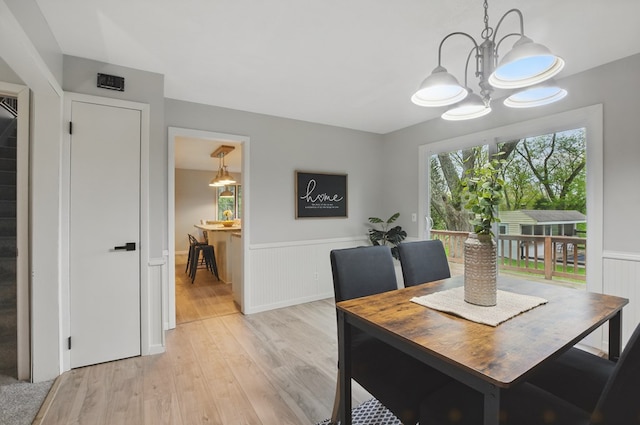 dining space featuring a wainscoted wall, light wood-type flooring, and a chandelier