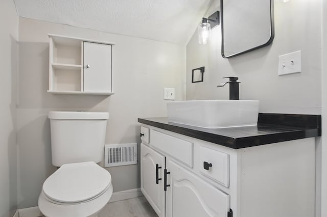 bathroom featuring vanity, toilet, a textured ceiling, baseboards, and visible vents