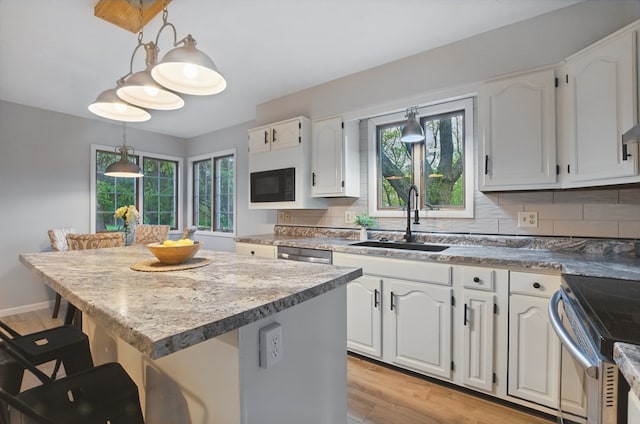 kitchen with a kitchen bar, decorative light fixtures, a center island, light wood-type flooring, and a sink