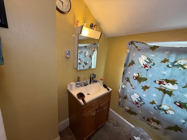 bathroom featuring lofted ceiling, stone finish flooring, vanity, and baseboards