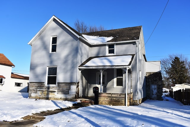 snow covered back of property featuring covered porch