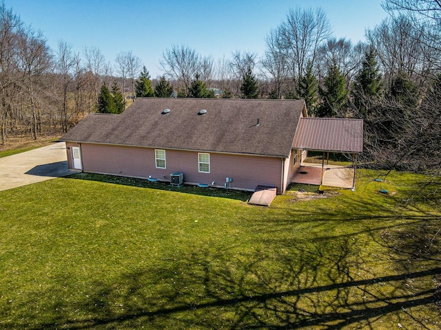 rear view of property with central air condition unit, concrete driveway, a yard, and a shingled roof