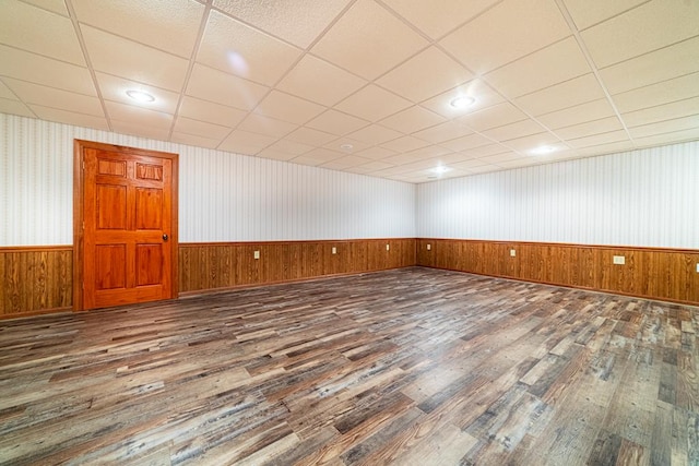 empty room featuring wooden walls, a wainscoted wall, a drop ceiling, recessed lighting, and wood finished floors