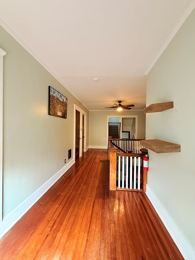 hall with baseboards, ornamental molding, hardwood / wood-style flooring, and an upstairs landing