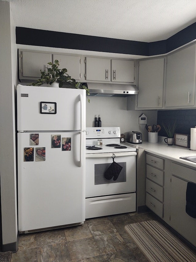 kitchen with white appliances, light countertops, stone finish floor, gray cabinets, and under cabinet range hood