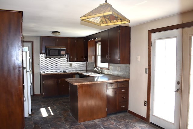 kitchen with black microwave, a peninsula, a sink, backsplash, and stone finish flooring