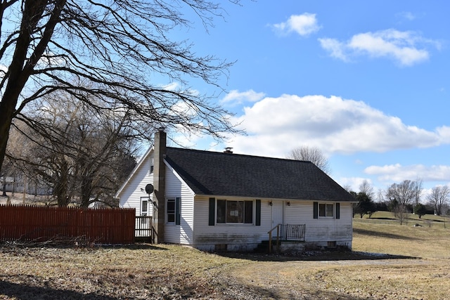 view of front of home with a shingled roof, a chimney, a front lawn, and fence